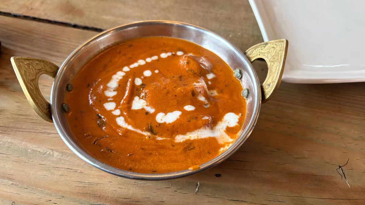 Butter chicken v mosazné pánvi kadai na dřevěném stole, fotografie, avif