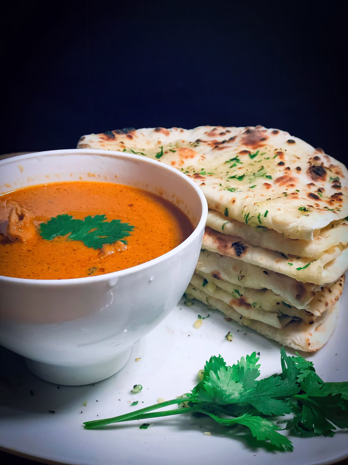 Miska butter chicken se stohem naanu na tmavém pozadí, fotografie, avif